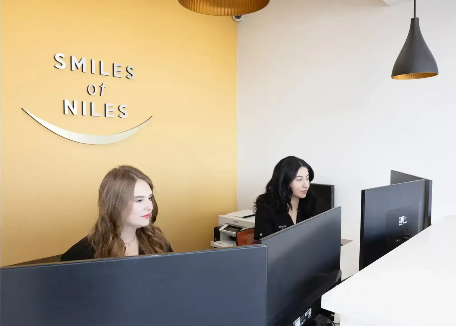 Two women at a front desk beneath a 