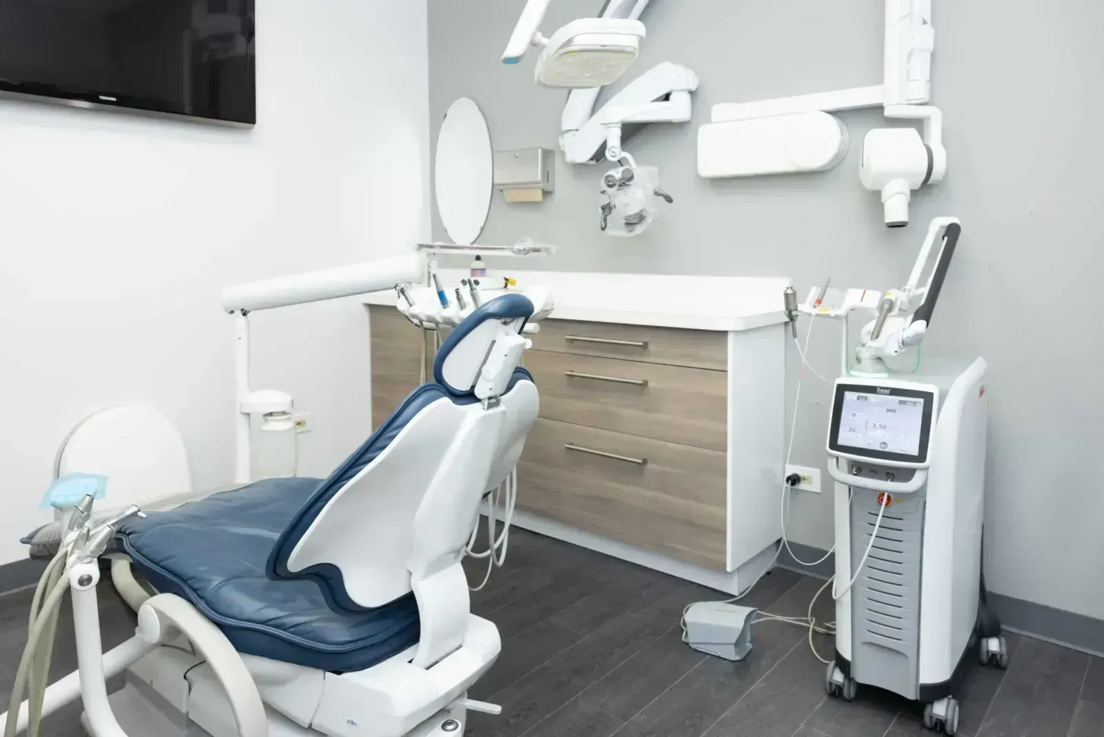 A modern dental treatment room with a chair, overhead light, and dental laser device.